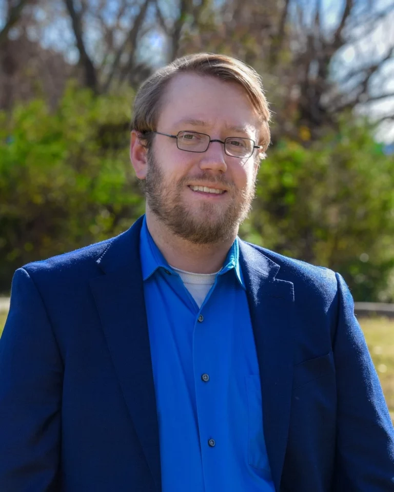 Nick Gausling wearing a monochromatic blue suit and dress shirt in a park in 2022